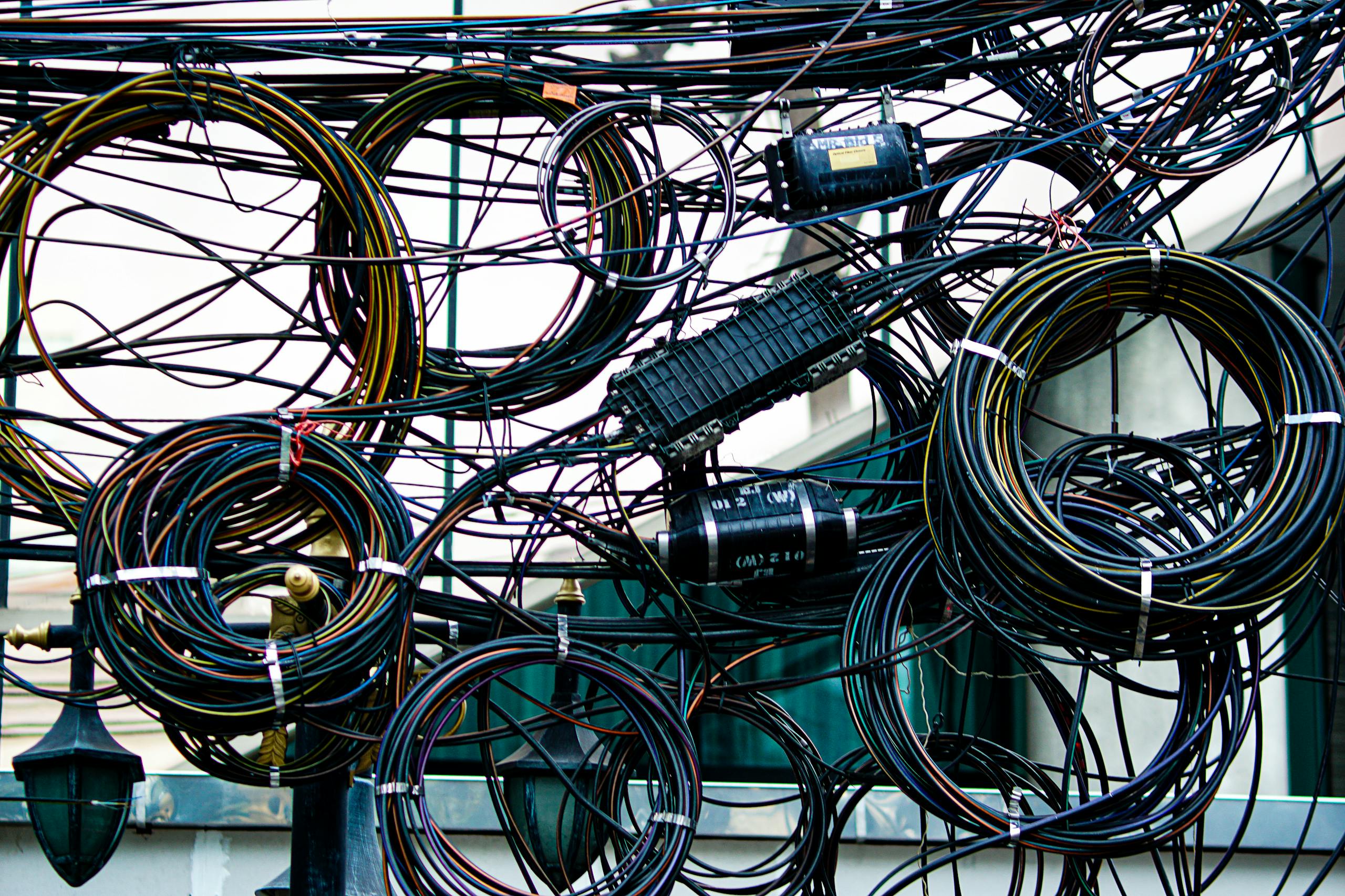 Intricate network of tangled power and communication cables outdoors.