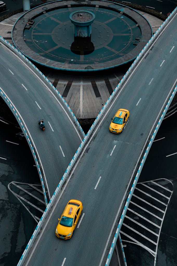 Aerial photograph of yellow taxis navigating a modern city overpass.