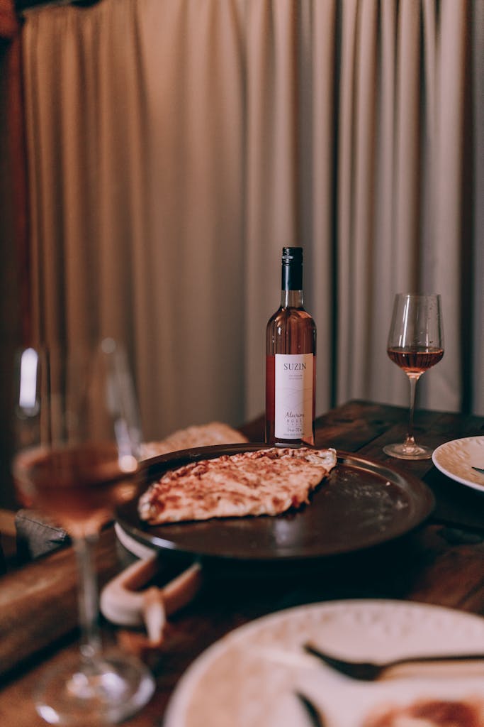 Warm indoor dinner scene featuring wine, pizza, and elegant glassware on a wooden table.