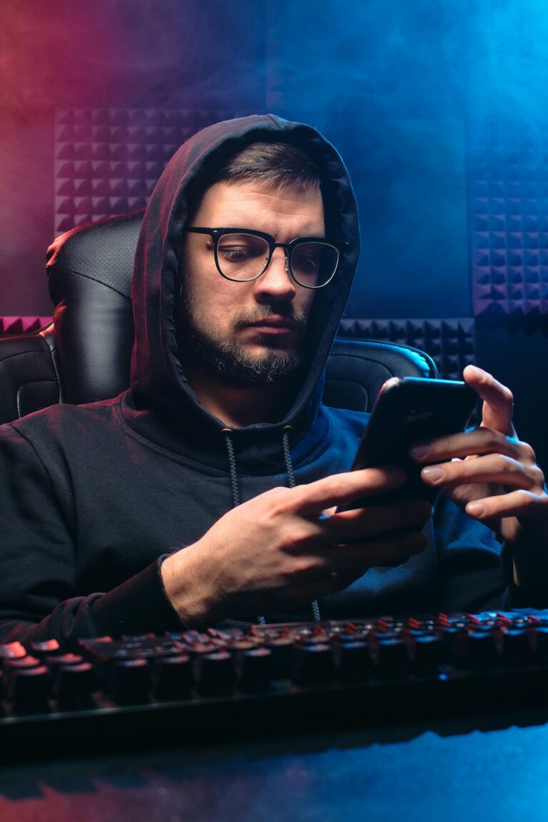 Man in hoodie using smartphone, representing cybersecurity themes like hacking and privacy.