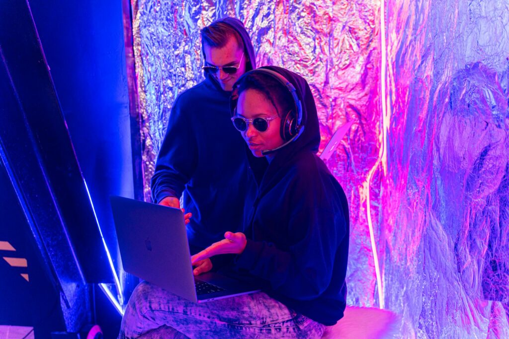 Two individuals in a neon-lit room work on a laptop, showcasing modern technology themes.