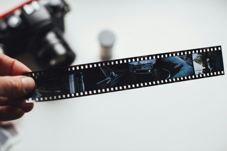 Close-up of a hand holding a vintage film strip with a blurred camera in the background, evoking nostalgia.